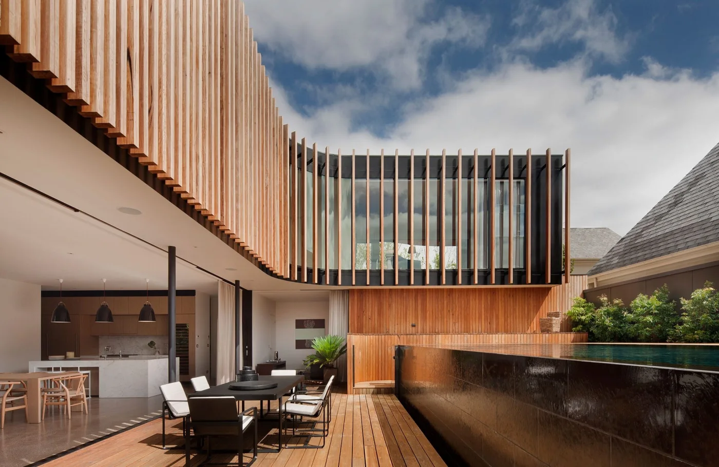 Modern timber-clad outdoor living space with a covered patio, dining area, and infinity-edge pool